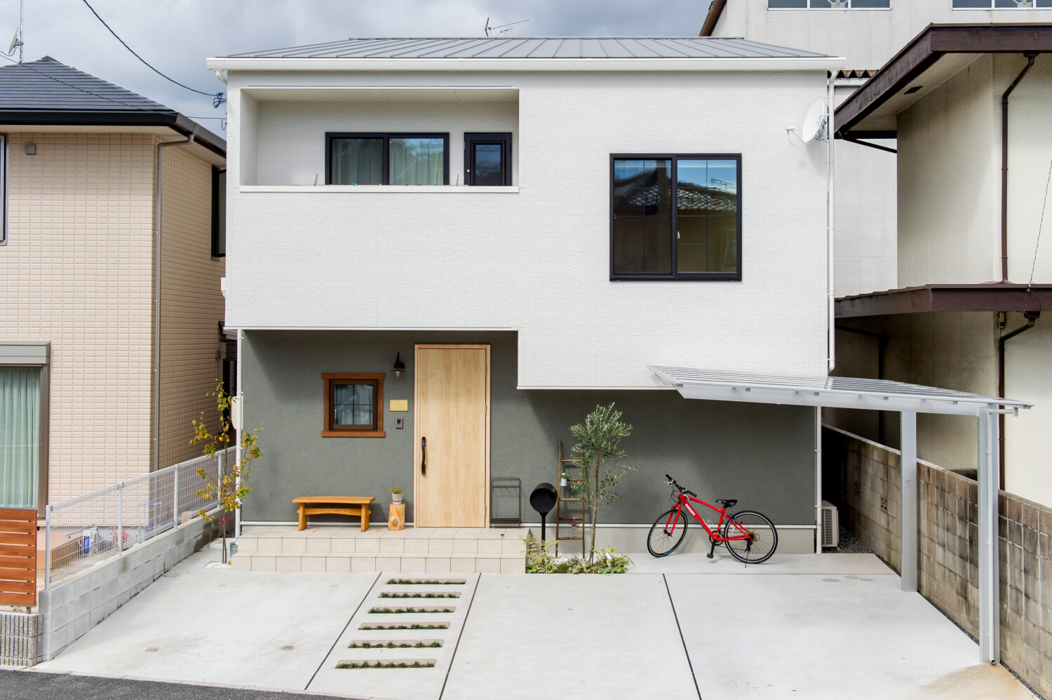 広島県の注文住宅　広島県廿日市市の建築実例　広島県で注文住宅ならアイデザインホーム　白とグレーの外壁に赤い自転車が置いてある家　木目柄の玄関ドアのある家