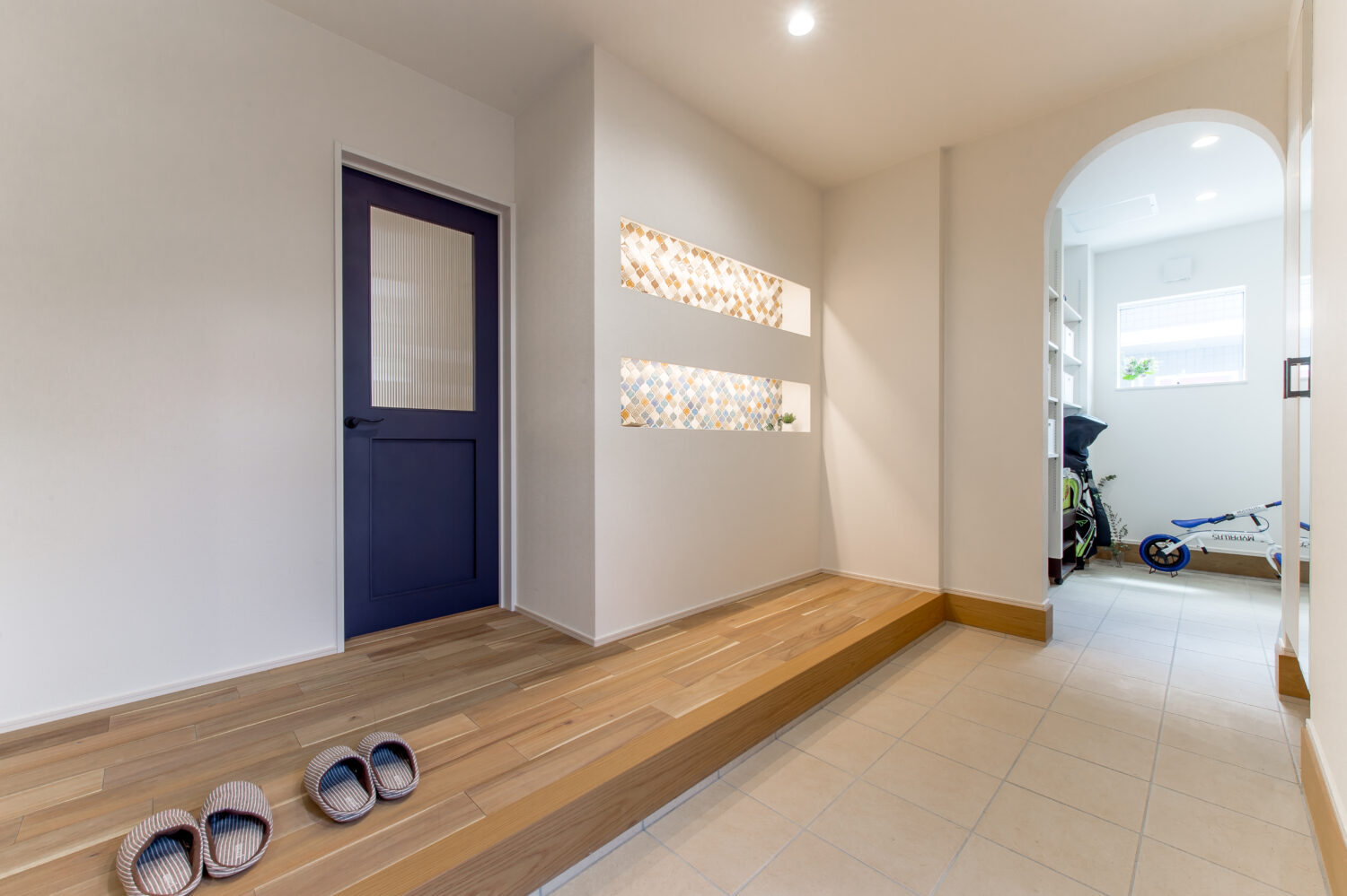 広島の注文住宅ならアイデザインホーム｜青いリビングドアと土間収納の入口にアーチ型の下がり壁のある玄関ホール