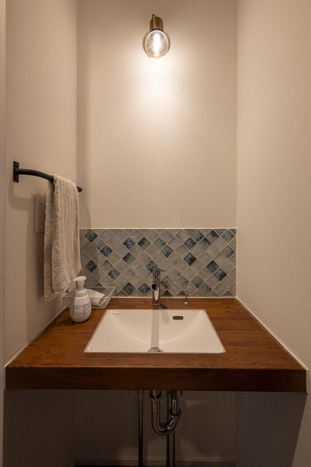 アイデザインホーム
三重の注文住宅　実例
木目のセカンド手洗いカウンターは淡いブルーのタイルが目を引く。
玄関から続くホールにあるため来客時や帰宅時に便利に活用できる。
アイアンのタオル掛けがアクセントとなっている。