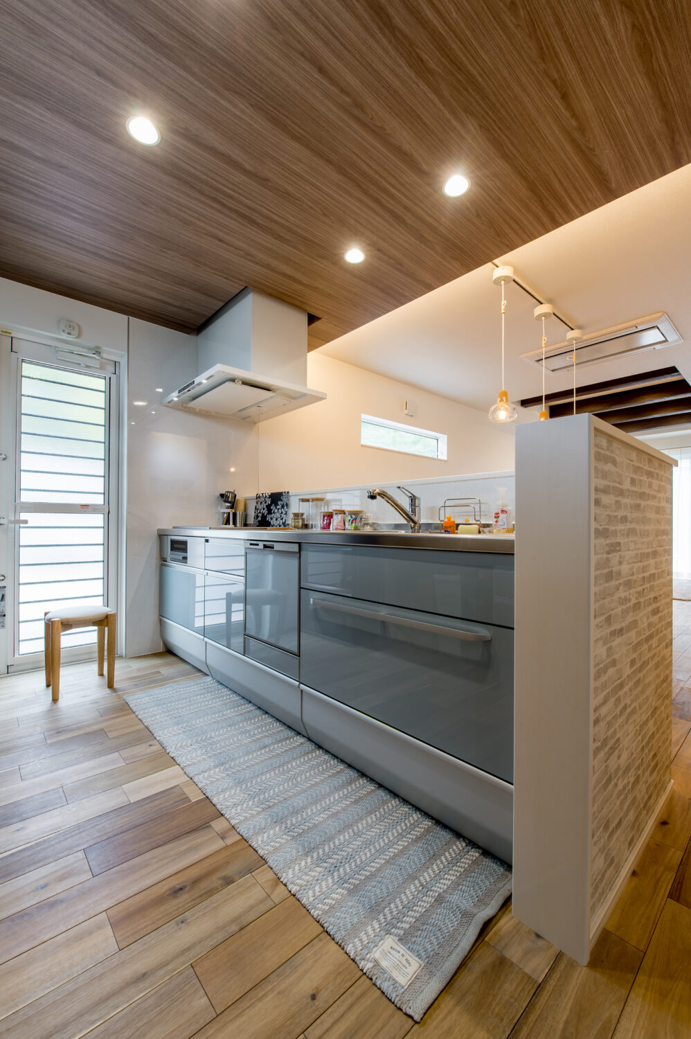 広島の注文住宅ならアイデザインホーム｜グレーで光沢のある扉を採用したスタイリッシュな印象を与えるキッチン。木目柄の天井で合わせた空間はナチュラルモダンなテイストです