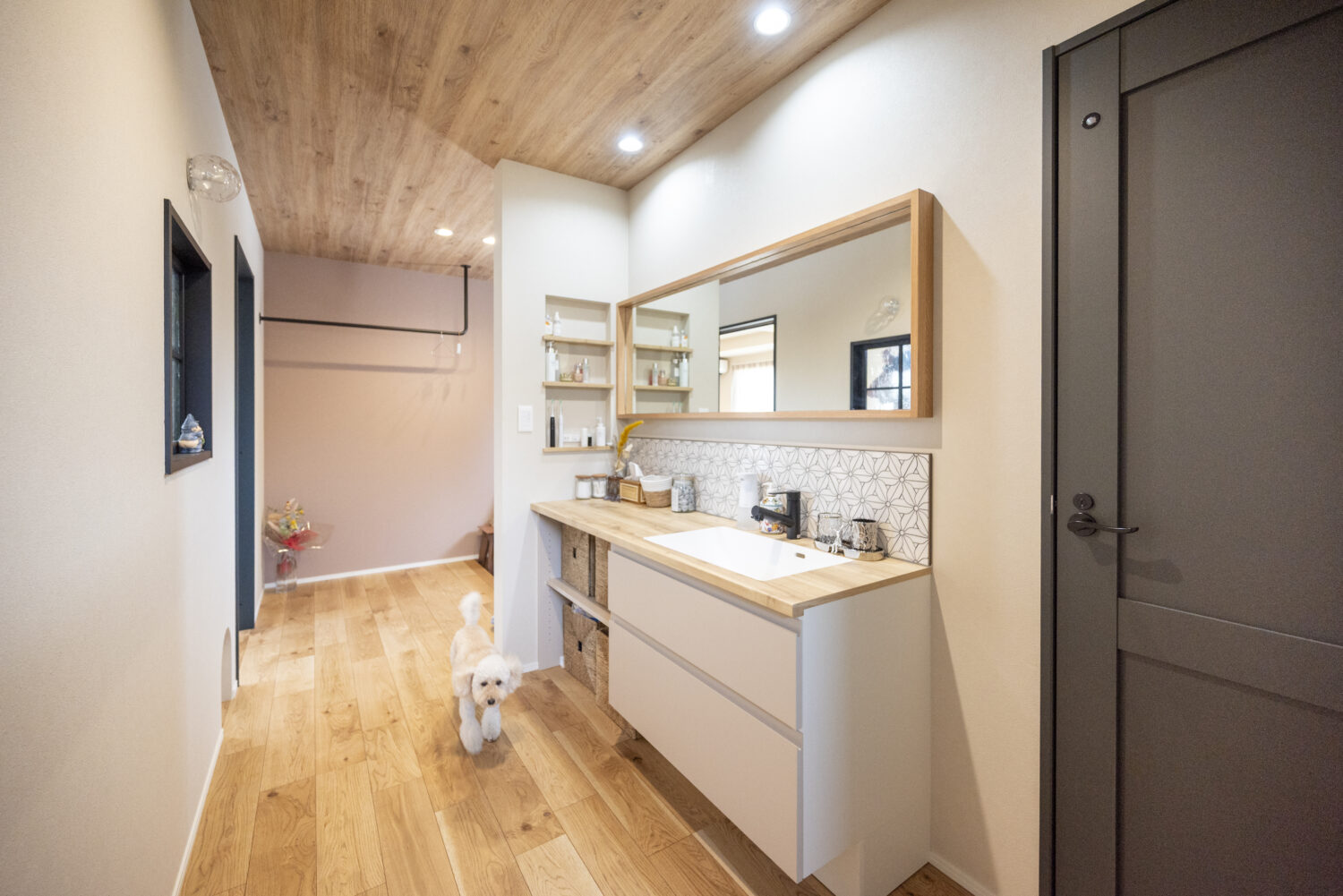 愛犬と暮らすピットリビングのあるジャパンディスタイルの家|アイデザインホーム 2人並んでも使いやすいワイドな鏡を設置した造作洗面台の前を、愛犬のりんちゃんが歩いている様子