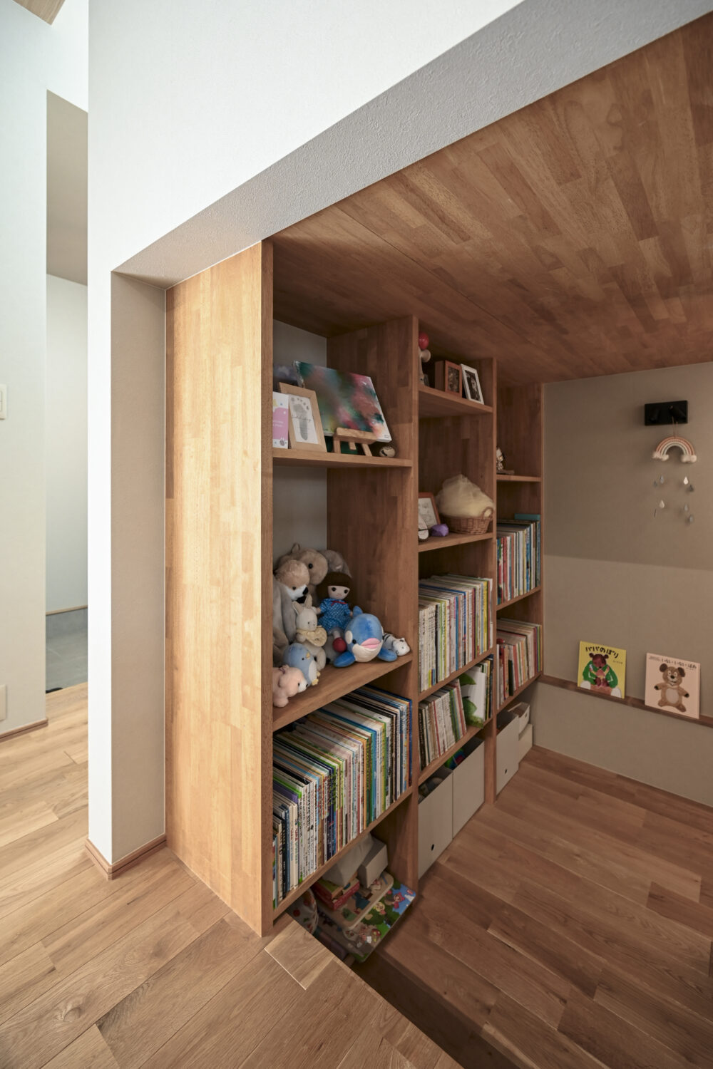 家族のこだわりが詰まった箱型ヌックと回遊動線のある家｜アイデザインホームの施工事例｜階段下には、絵本がずらりと並ぶ造作本棚を備えたヌックを計画
